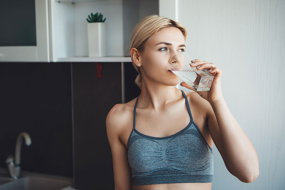 lovely-caucasian-woman-with-blonde-hair-wearing-sportswear-is-drinking-glass-water-digital-fitness-lessons-home